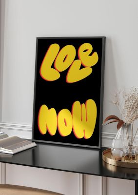 An unframed print of love now black graphical in typography in yellow and black accent colour